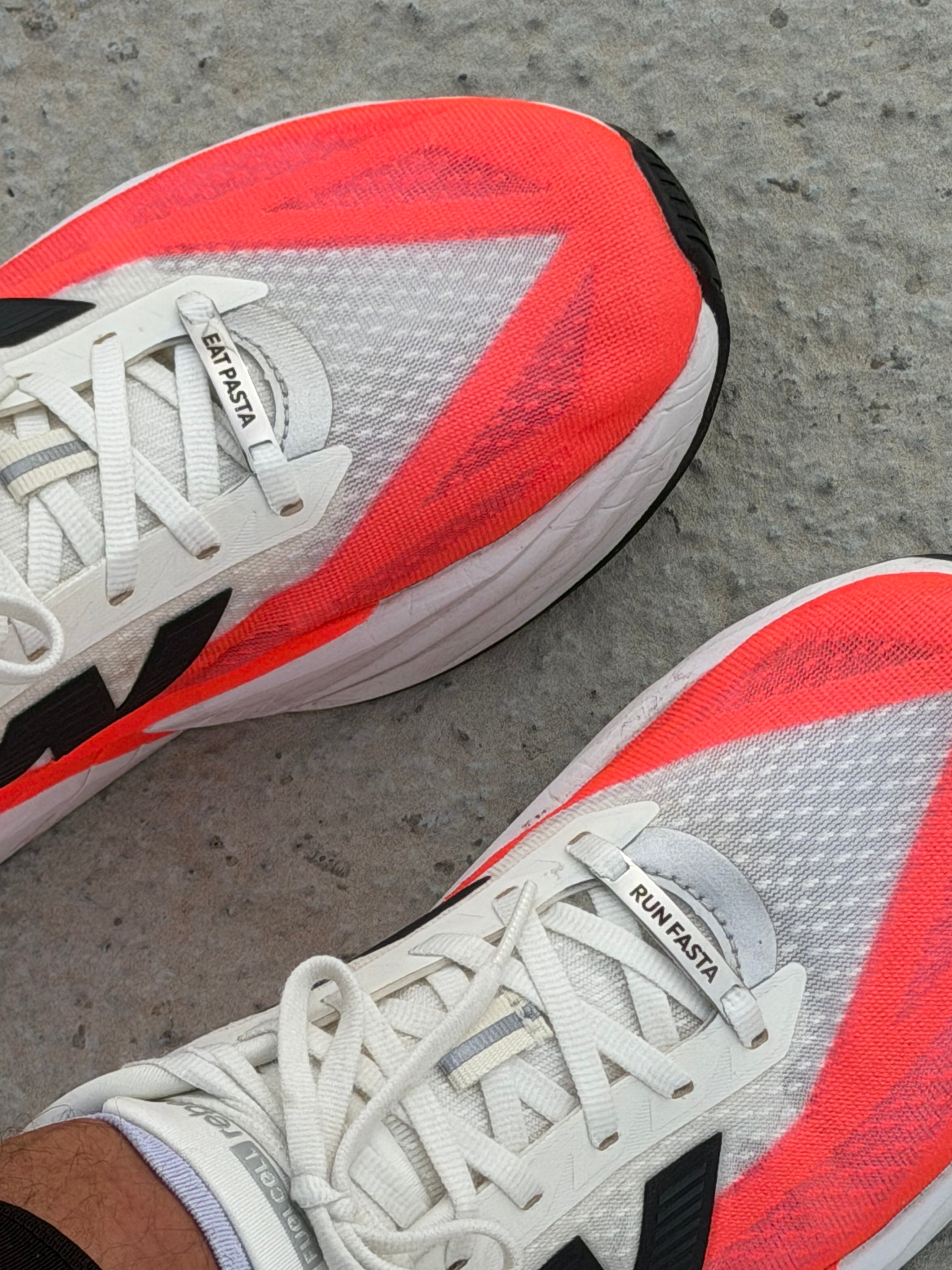 Shoe Tags Momenta EAT PASTA et RUN FASTA installés sur une paire de chaussures de running blanches.